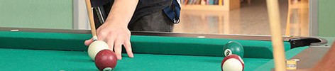 Das Bild zeigt zwei Männer, die Billard spielen. Im Hintergrund ist ein Bücherregal zu sehen.
