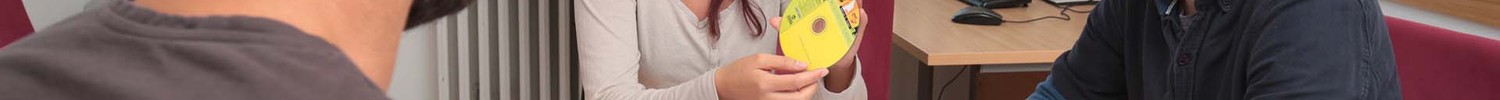 Eine junge Frau und zwei junge Männer sitzen an einem Tisch und unterhalten sich